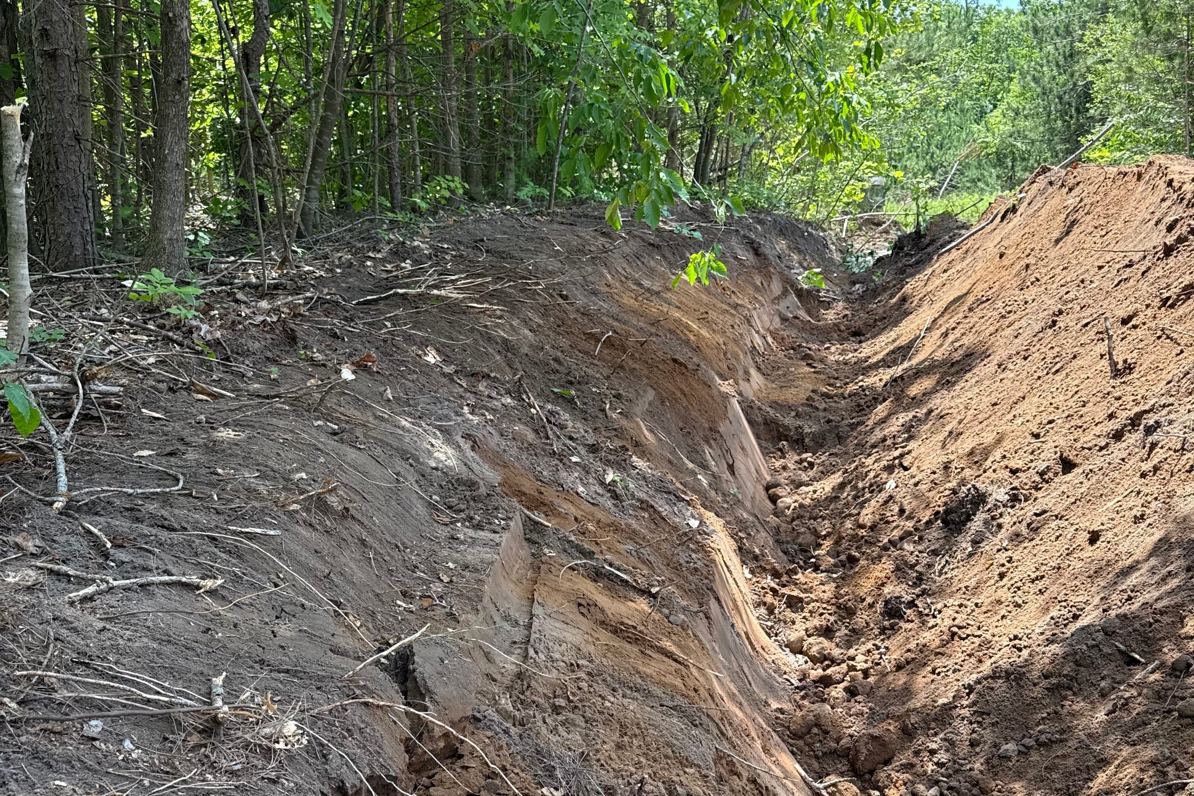 Freshly excavated drainage trench through a wooded property