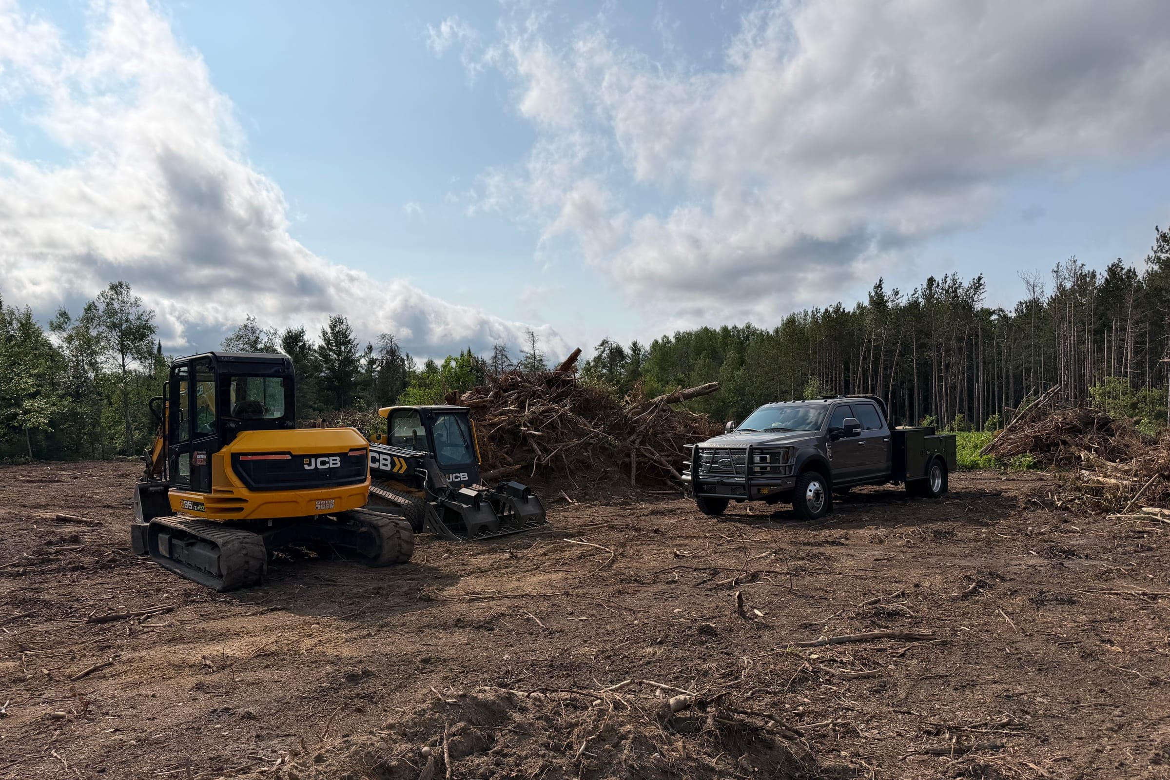 Northern Dirt equipment clearing a large pile of trees and storm debris