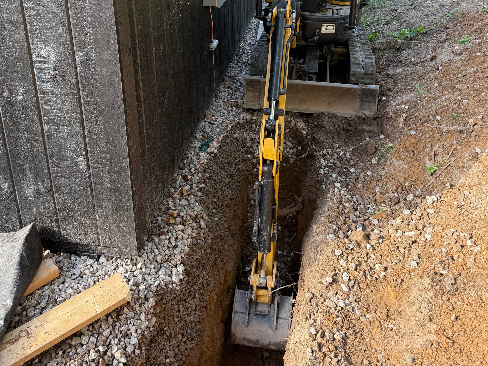 Compact excavator digging a precise trench beside a structure